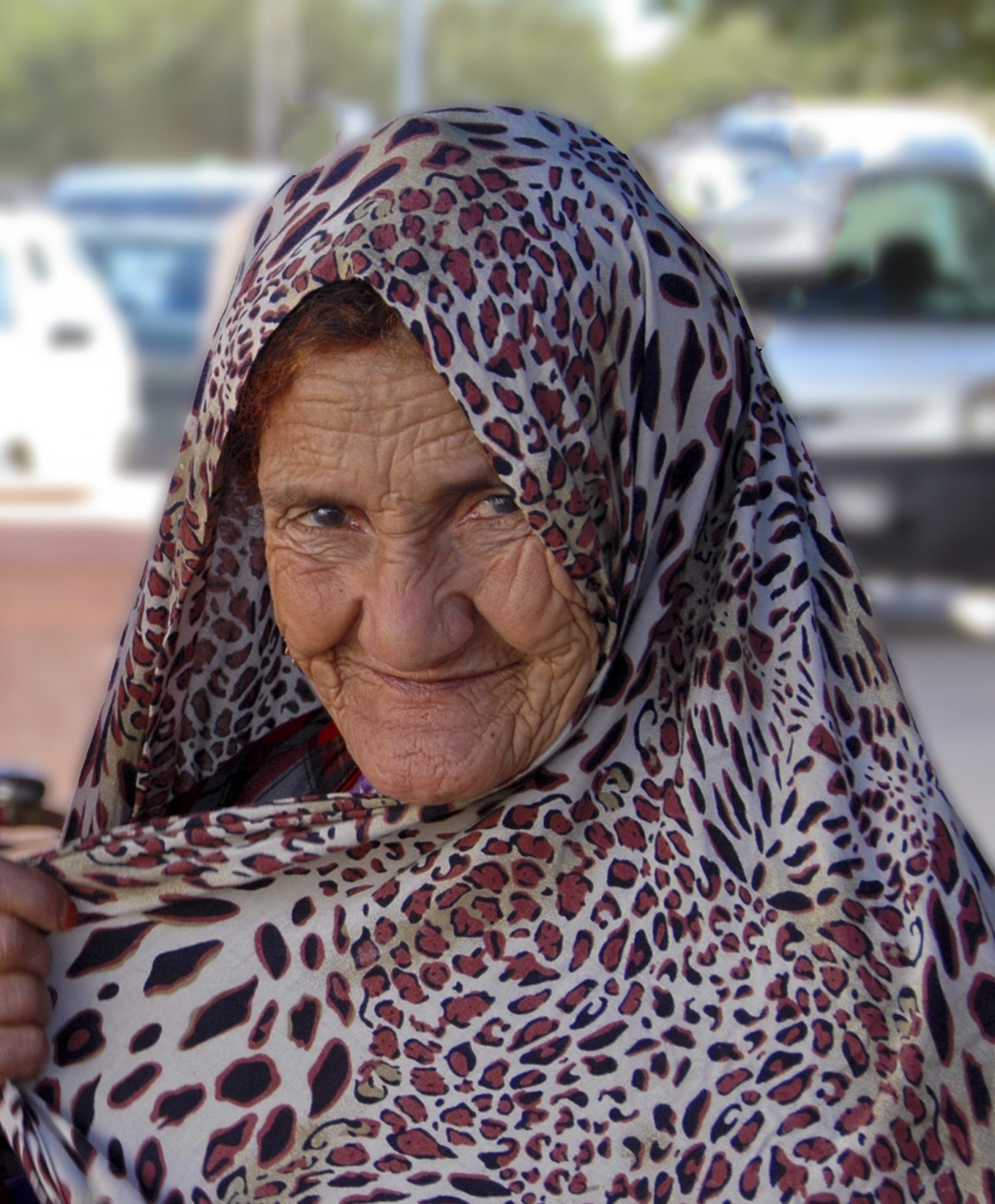 An elderly woman wearing a leopard print headscarf smiles