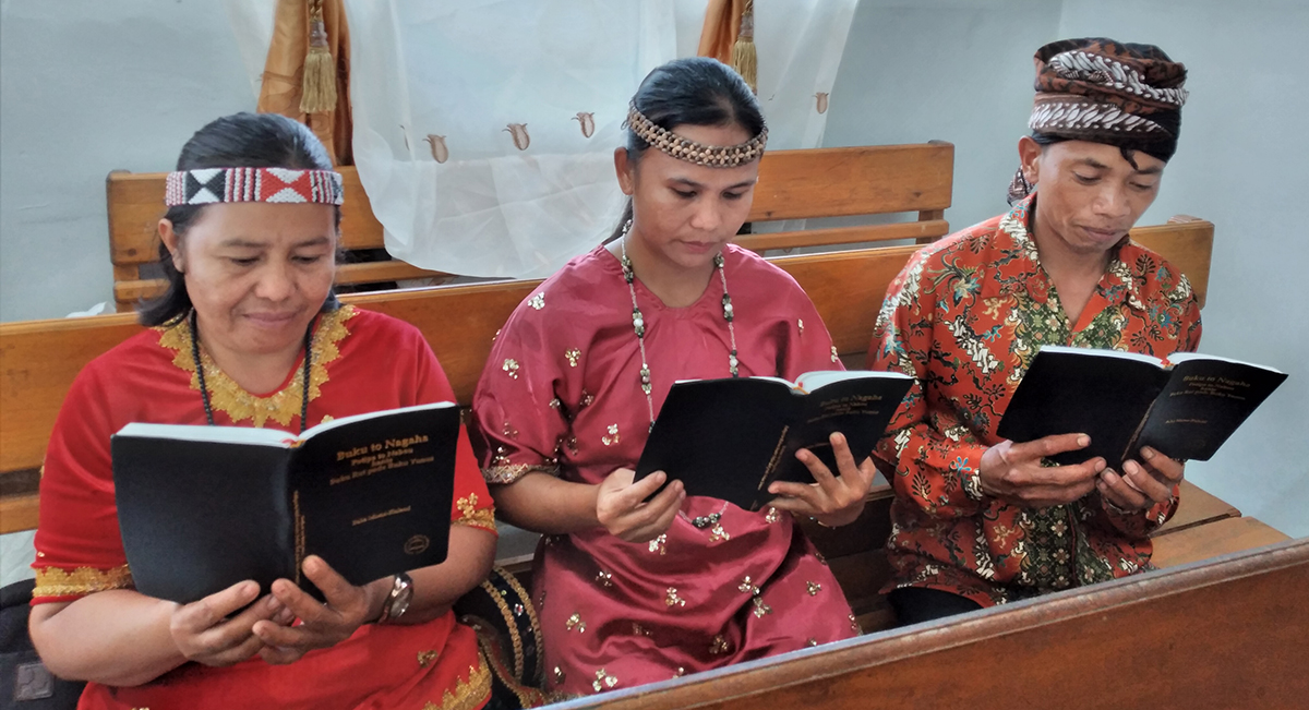 Image of three Moma people reading their newly launched New Testaments