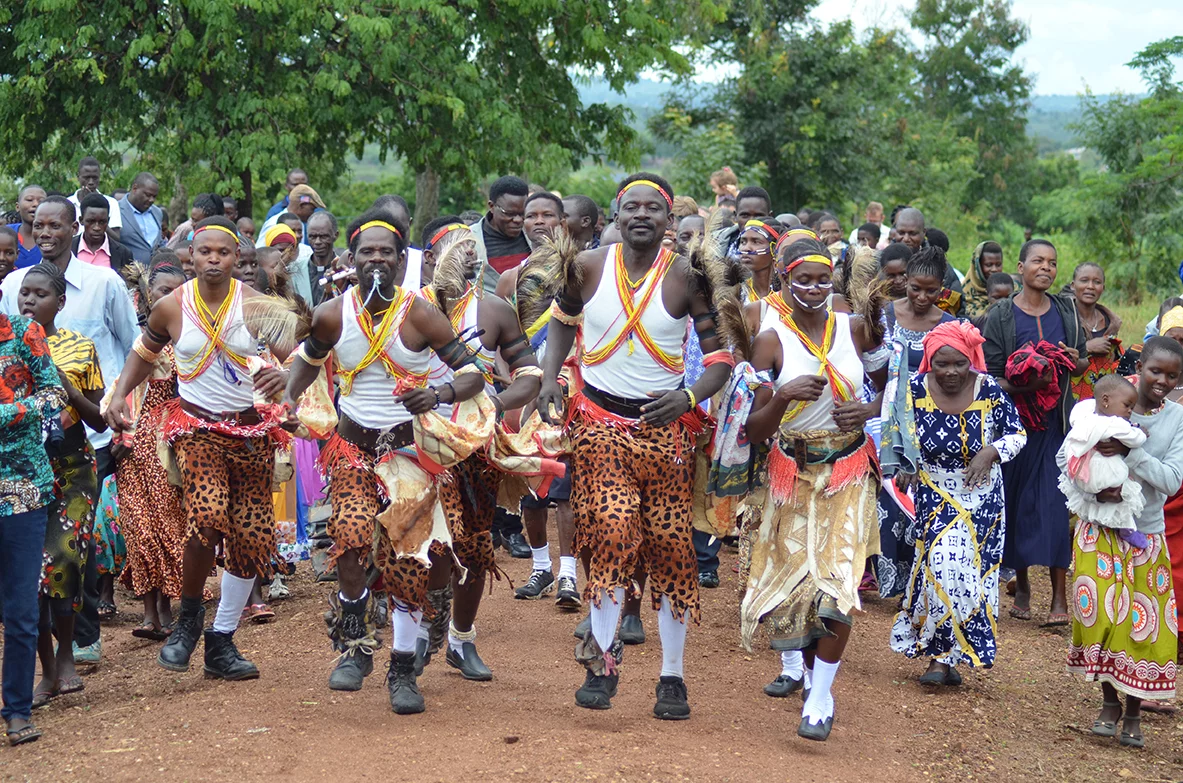 Image of a group in traditional dress leads the crowd in the street parade, singing and dancing from the village market to the church.
