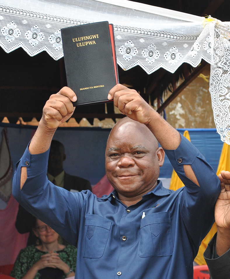 Image of Nyiha Bible translator and pastor Wilhelm Mwakavanga holds up the Nyiha New Testament at its launch event on 17 May 2023 in Tanzania