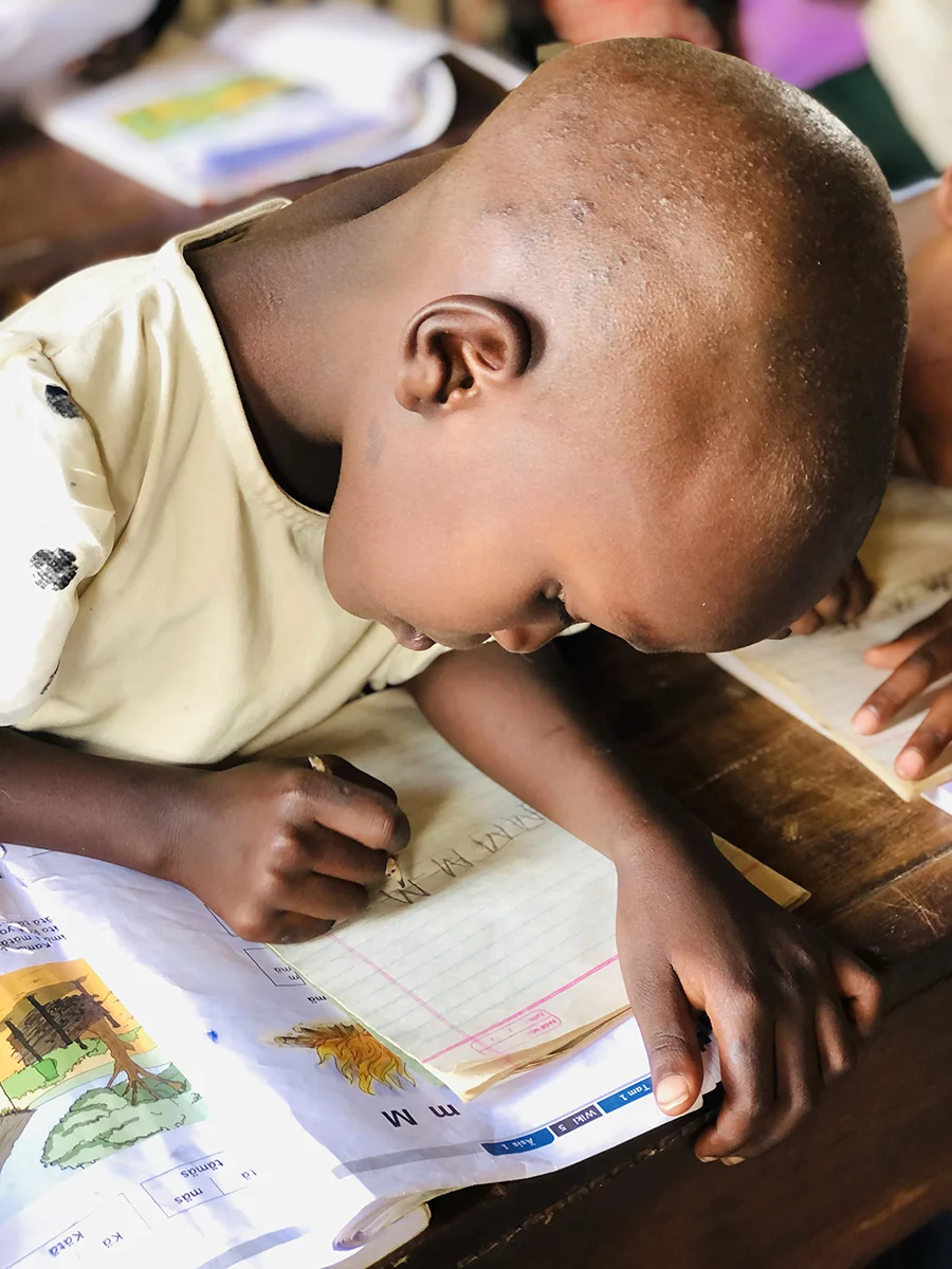 Image of a Pokot child writing in their book during a school class