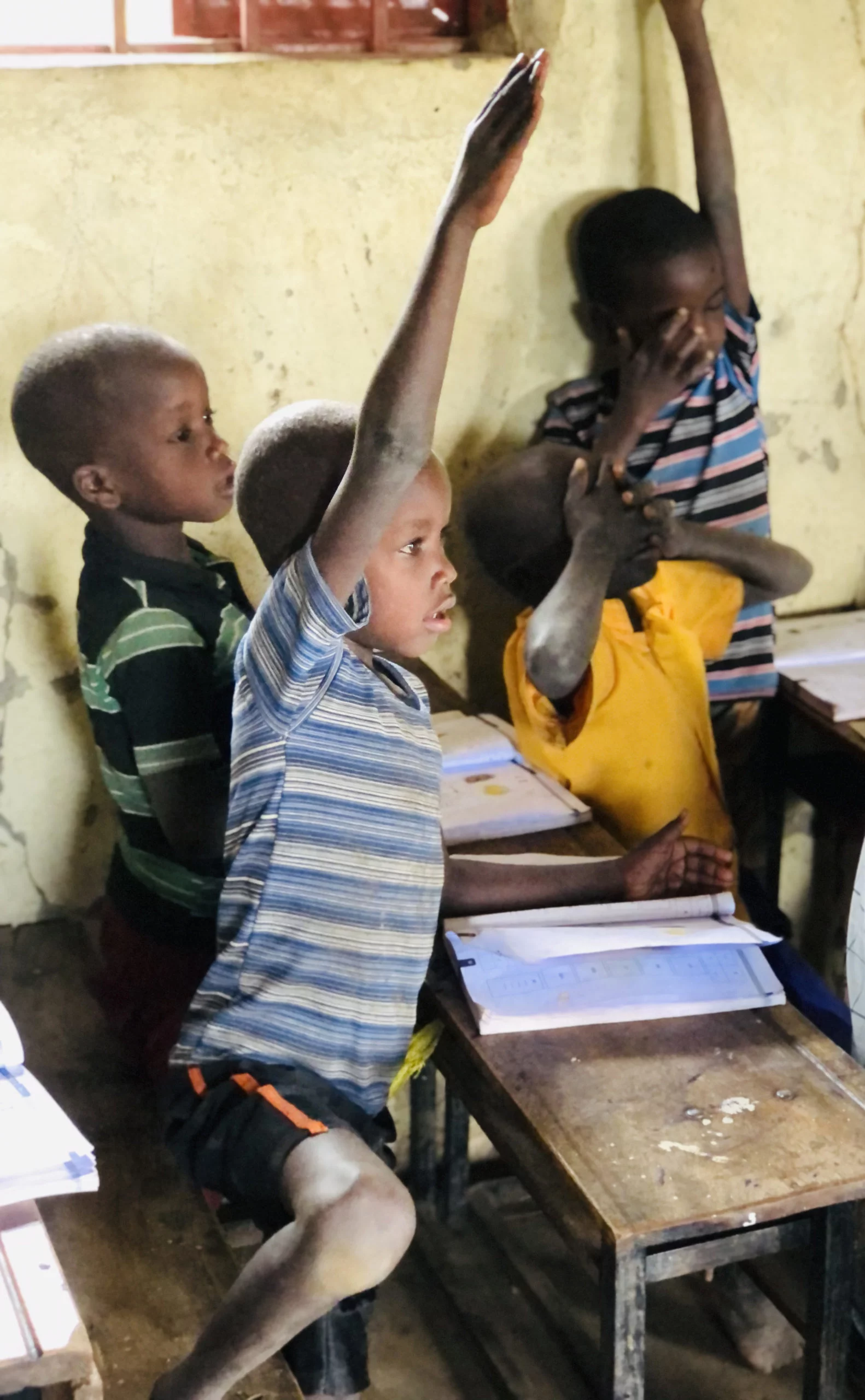 Image of Pokot children with arms up high to answer a question during school class