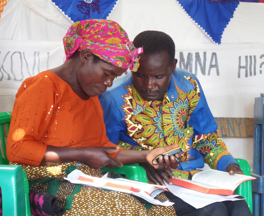 Image of two Malila people comparing the New Testament in print and audio forms at a workshop