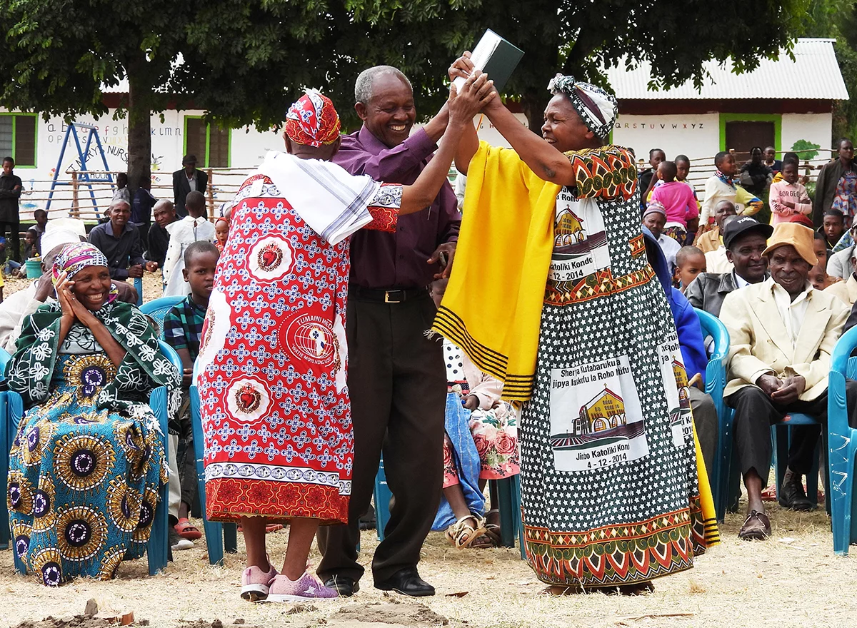 Image of three people dancing with their Rangi New Testament at its launch